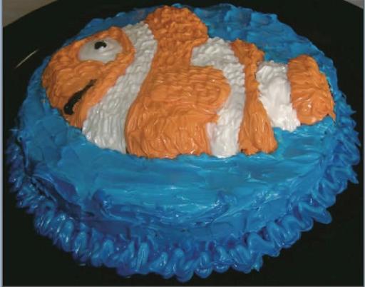 Clownfish Cake.jpg - For a fish-lover's birthday, make a clownfish cake. Press a 1-inch layer of clay into the bottom of round, deep pan. Remove a portion of the clay in the center of the pan in the shape of a clownfish. If you want the orange and yellow segments to be slightly different heights, add small layers of clay where the white segments will be. Spray the pan and clay with cooking spray, and pour cake batter such that the batter is about 3/4-inch above the highest portion of the clay. Bake until done, loosen the cake from the sides of the pan, and invert the pan. To make the wavy frosting, generously frost the cake. Then lightly press a spoon into the icing and lift it up away from the cake.Added by: Admin.